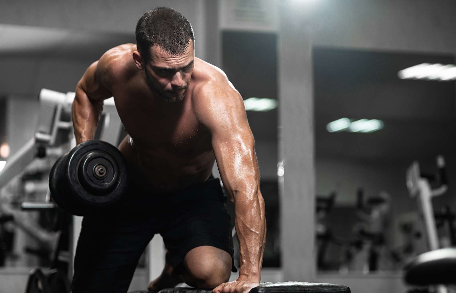 A man trains in the gym. Athletic man trains with dumbbells, pumping his biceps