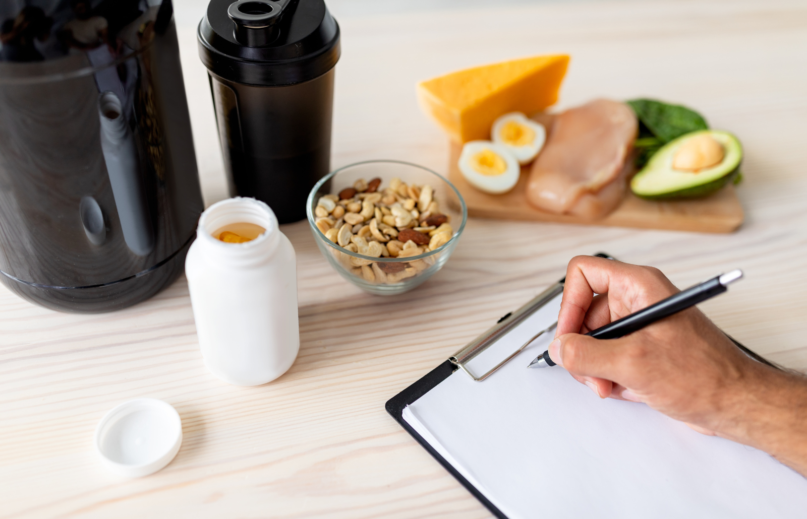 Cropped view of young bodybuilder writing meal plan on clipboard with mockup, eating healthy foods, using sports supplements and protein shakes on wooden table, closeup