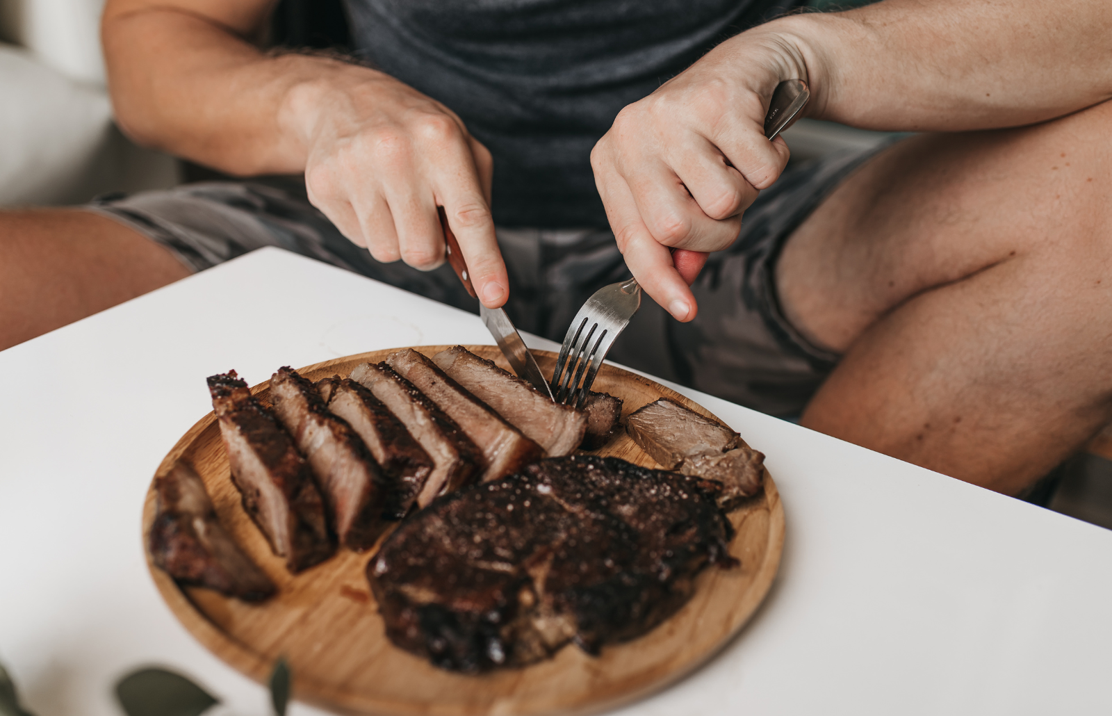 A man eating rib eye steak from a wooden plate - Carnivore Diet