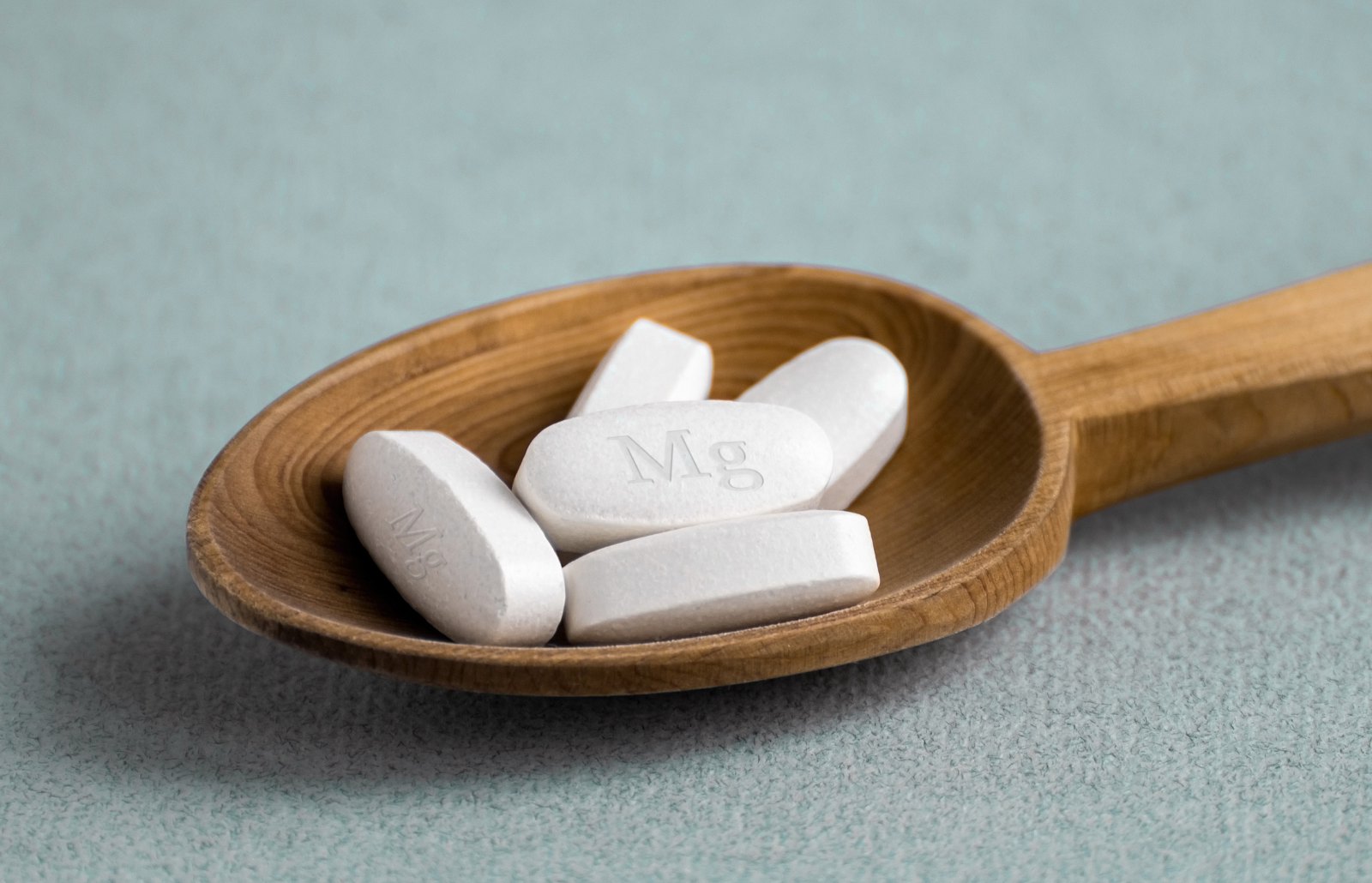 Tablets , vitamins with the abbreviation Mg ( magnesia, the macronutrient magnesium ) lying in a wooden spoon on a light background.