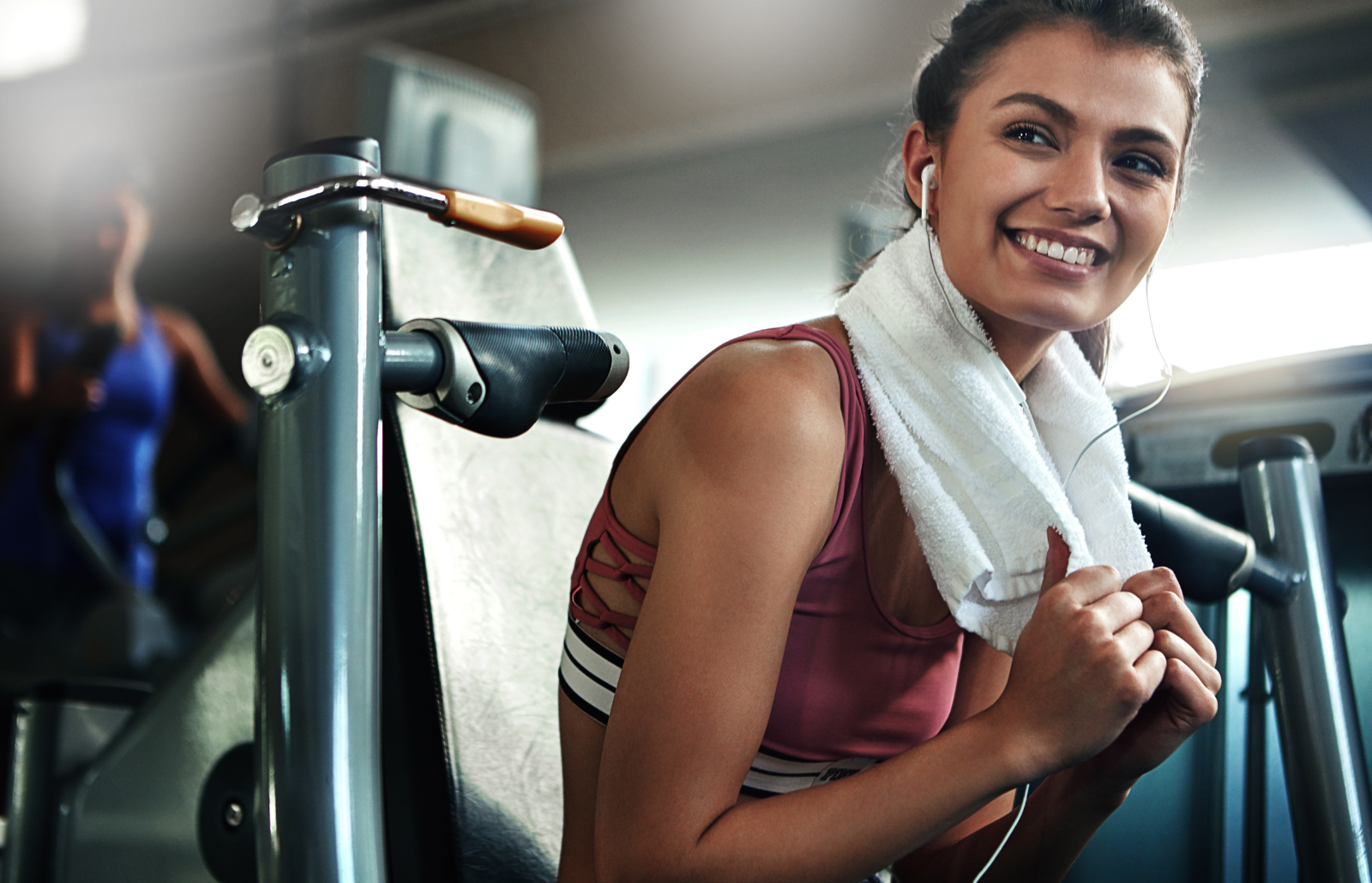 Gym, towel and woman with smile, fitness break and warm up for intense weight performance. Sport, earphones and female athlete ready for workout, training and chest press exercise for strength